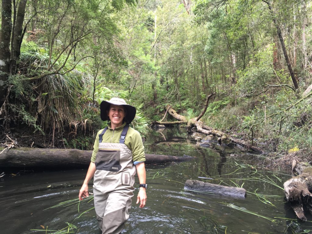 Photo of Krista in her waders standing in a forested stream