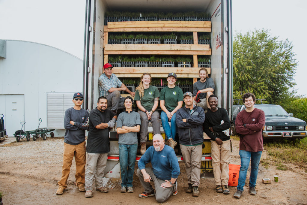 Volunteer and staff from OneCanopy posing by a truck filled with racks of seedlings.